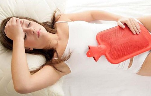 Kobieta leżaza na łóżku z termoforem, miesiączka