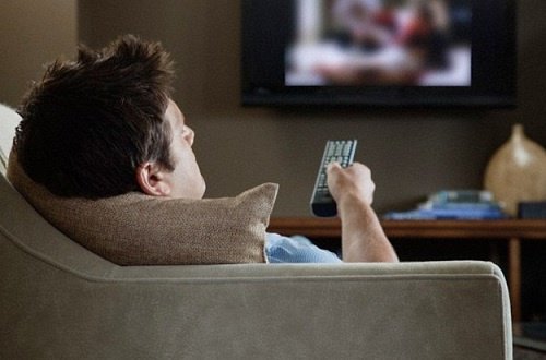 Mężczyzna w fotelu ogląda telewizję w pozycji wywołującej ból szyi