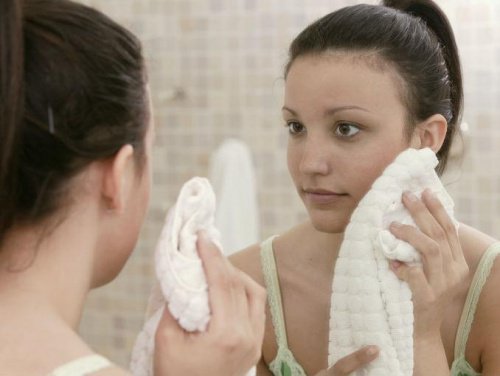 Kobieta wyciera twarz ręcznikiem przed lustrem