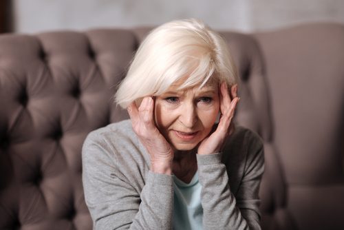 Starsza kobieta trzyma się za głowę - choroby neurodegeneracyjne