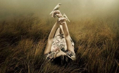 Kobieta leży na łące i trzyma w dłoni ptaki