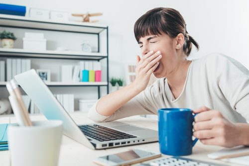 ziewająca kobieta siedząca przed komputerem - zaburzenia hormonalne