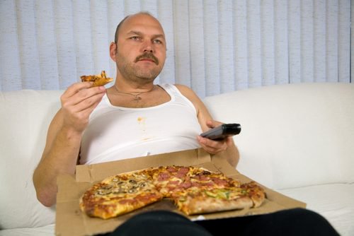 Mężczyzna z pizzą na kolanach i pilotem w ręce