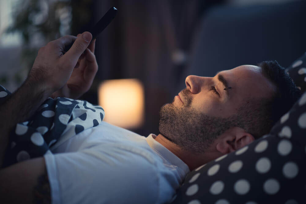 Mężczyzna sprawdzający telefon przed snem - przykład na szkodliwość telefonów komórkowych