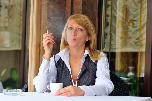 Kobieta pije kawę i pali papierosy.