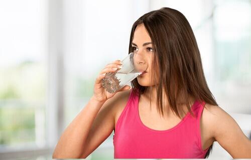 Kobieta pije wodę aby nawodnić organizm