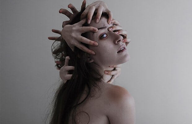 Kobieta z wieloma dłońmi na głowie.