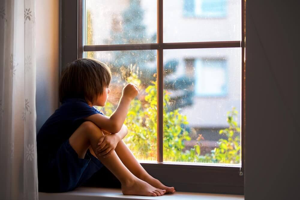 Dziecko patrzące przez okno i jego traumy emocjonalne