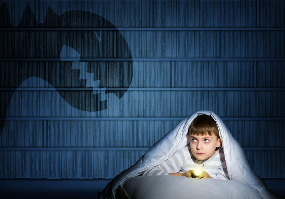 Chłopiec w łóżku z latarką i potwór na ścianie