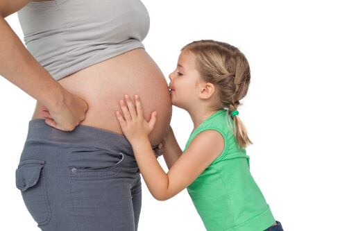 Dziewczynka całuje brzuch mamy w ciąży