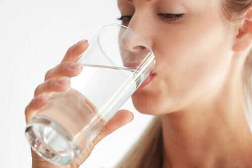 Kobieta pije wodę ze szklanki, prawda o pielęgnacji skóry