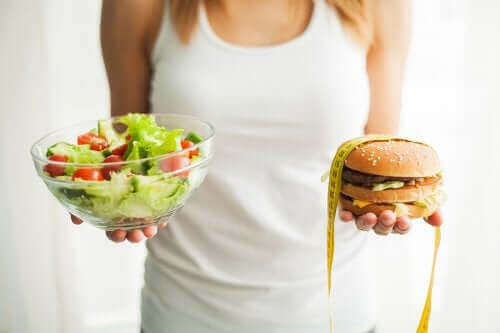 Kobieta trzymająca sałatkę i hamburgera - jak ochronić się przed otyłością