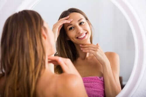 Uśmiechnięta kobieta oglądająca swoją twarz w lustrze - warto zmywać makijaż przed snem